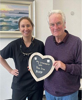 A dentist and a patient holding a board reading "my treatment was pain free #SRDP"